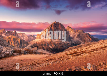 Mountains at sunset in Dolomites, Italy. Landscape with high rocks, stony trail, small house, purple sky with pink clouds in the evening. Autumn scene Stock Photo