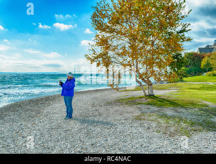 Woman standing on stony beach on Mackinac Island taking picture of waves Stock Photo