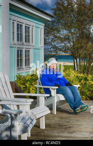 A woman sitting in an Adirondack chair on a dock on a lake 