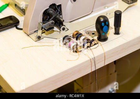 box with metal spools of colored threads near sewing machine. Tailor industry concept.designer atelier, tailoring process concept.Workplace of tailor,colorful spools of threads on table with mess in atelier Stock Photo