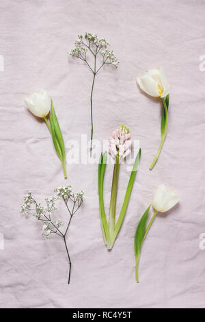 Spring, Easter floral botanical composition. White Gypsophila, tulips and hyacinth flowers lying on pink linen tablecloth background. Styled stock photo. Vertical flat lay, top view. Stock Photo