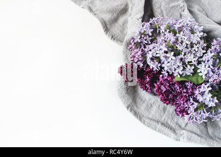 Easter styled stock photo. Spring feminine scene, floral composition. Decorative banner, corner made of beautiful purple lilac flowers on linen napkin. White table background. Flat lay, top view. Stock Photo