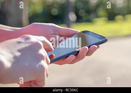 Black smartphone in hand in the park outdoors, lit by the sun. Technologies in everyday life and business Stock Photo