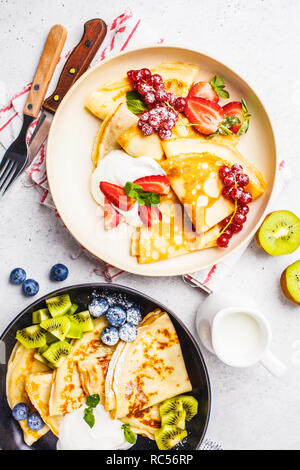Homemade thin crepes served with curd cream, fruits and berries in black and white plates. Healthy beautiful breakfast concept. Stock Photo