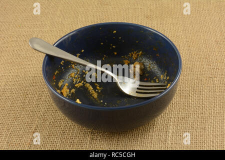 Empty blue bowl with fork with last remnants of cheese grits at end of meal Stock Photo