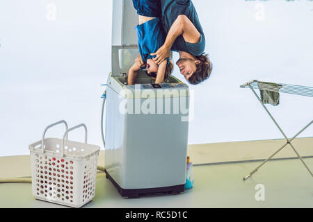 Father tries to wash his son in a washing machine standing upside down with his feet Stock Photo