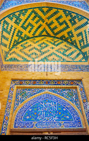 The intricate decorative details of the small portal (iwan) of Jameh Mosque with Islamic patterns of azure tiles and Quranic calligraphy, Yazd, Iran. Stock Photo