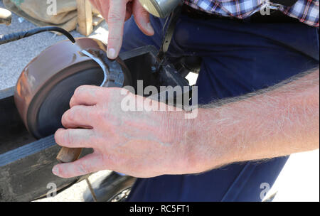 knife sharpener sharpens the blade of an old bill hook using a grinding wheel Stock Photo