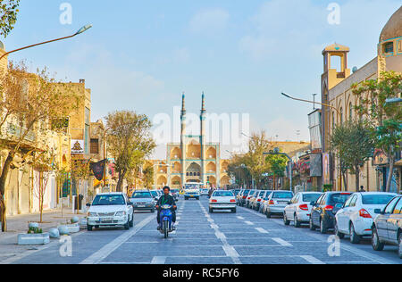 YAZD, IRAN - OCTOBER 18, 2017: Fast traffic in Qiyam street with mullah (Islamic cleric), riding on the bike and medieval Amir Chakhmaq complex on bac Stock Photo