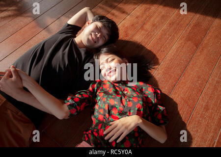 asian younger man and woman lying on wood floor with happiness face Stock Photo