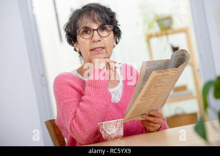 beautiful brunette mature woman dressing in pink reading a newspaper Stock Photo