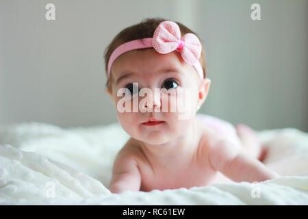 Cute baby girl laying on the bed, with a bow on her hair Stock Photo