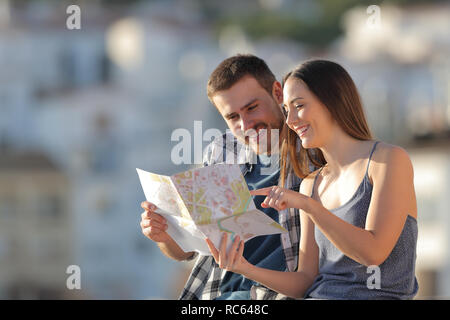 Couple of happy tourists checking paper guide in a town on vacation Stock Photo
