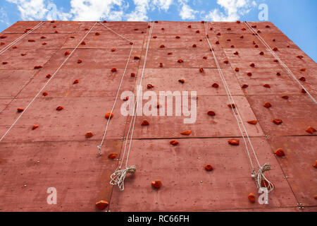 Artificial rock climbing wall with grips for hands and feet in outdoor adventure park used to practise lead climbing or bouldering Stock Photo