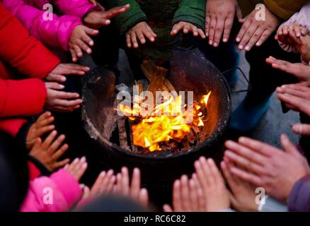 (190114) -- NANCHANG, Jan. 14, 2019 (Xinhua) -- Principal Zhang Zhanliang and students warm themselves by a stove fire at Huangni elementary school in Chuntao Town of Yujiang District of Yingtan City, east China's Jiangxi Province, Jan. 4, 2019. Zhang Zhanliang, the principal of Huangni primary school, has been known nationwide recently for taking care of the school's left-behind children, whose parents are migrant workers in towns and cities. For years, there's no canteen at Huangni elementary school. Appointed as principal in 2018, Zhang Zhanliang spent his own money cooking additional meal  Stock Photo