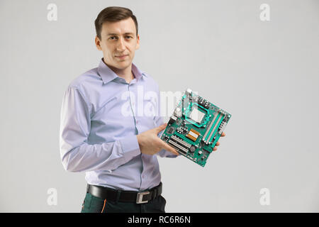 young man with motherboard in his hands is isolated on light background Stock Photo