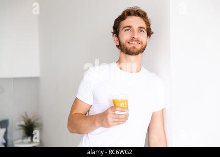 Image of a handsome young bearded man at home drinking juice. Stock Photo
