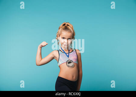 Cheerful little sports girl celebrating the win isolated over blue background, wearing a gold medal Stock Photo