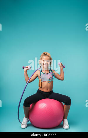 Cheerful little girl wearing sport clothes doing exercises with fitness  ball isolated over blue background Stock Photo - Alamy