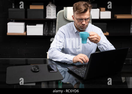 Serious businessman working on laptop and drinking coffee Stock Photo