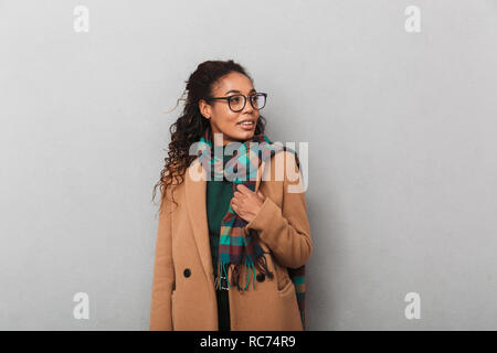 Smiling african woman wearing coat looking away at copy space over gray background Stock Photo