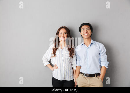 Cheerful asian business couple standing isolated over gray background Stock Photo