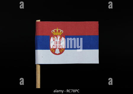 A national flag of Serbia on toothpick on black background. A horizontal tricolor of red, blue, and white with coat of arms. Stock Photo