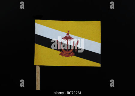 A official and unique  flag of Brunei on toothpick on black background. A centered red crest of Brunei on a yellow field cut by black and white diagon Stock Photo