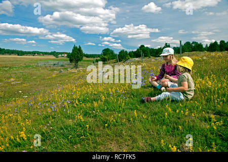 Two blond girls sitting on meadow Stock Photo