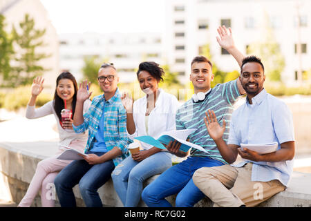 students with notebook waving hands outdoors Stock Photo