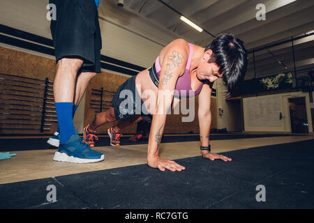 Trainer standing over pregnant woman doing push ups in gym Stock Photo