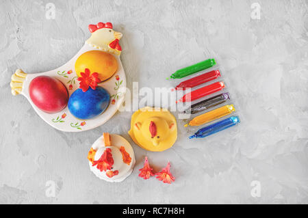 Multi-colored Easter eggs lie on a white plate in the shape of a chicken next to paint for coloring and Easter cakes. Copy space. Stock Photo