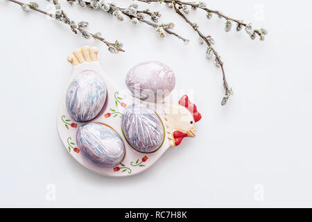 Multi-colored Easter eggs lie on a plate in the form of a chicken on a light background with a bouquet of willow branches. View from above. Easter Bru Stock Photo