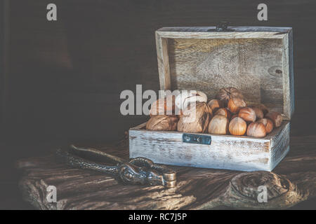 Pecan nuts and macadamia walnuts in a box with pegs for nuts on a wooden background. Copy space. Stock Photo