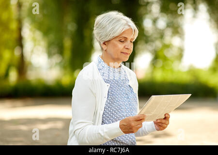 senior woman reading newspaper at summer park Stock Photo