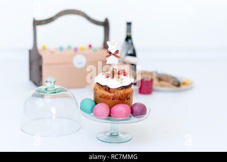 Easter cake, colored eggs and bottle of red wine. Easter composition with orthodox sweet bread, kulich and bottle of wine on light background. Gifts for holiday in wooden basket. Copyspace for text Stock Photo