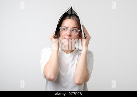 Portrait of young girl while studiyng covering head with book. She is tired and feeling stressed. Stock Photo