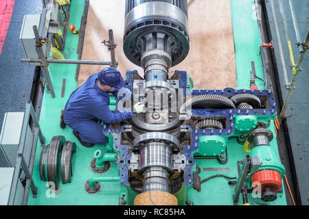Overhead view of engineer inspecting gears on generator in turbine hall of nuclear power station during outage