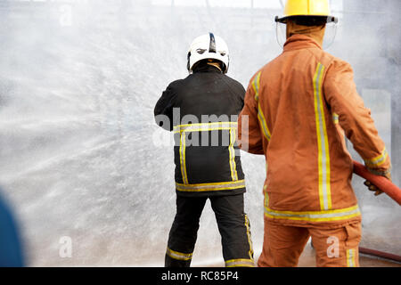 Firemen training, firemen spraying water at training facility, rear view Stock Photo