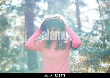 Young female runner putting on headphones in sunlit forest Stock Photo