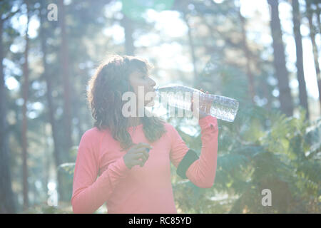 Young female runner drinking bottled water in sunlit forest