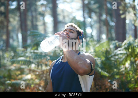 Male runner drinking bottled water in sunlit forest Stock Photo