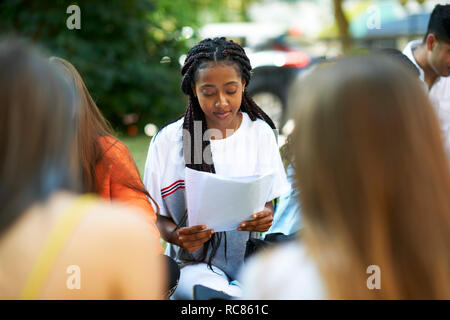 Male and female higher education student looking at paperwork on college campus lawn, over shoulder view Stock Photo
