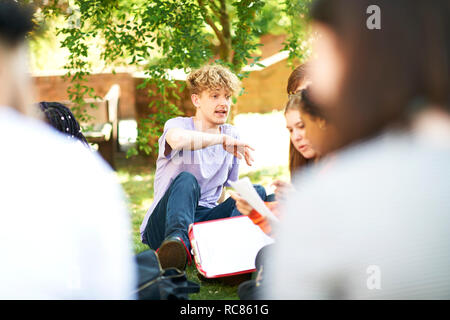 Male and female higher education students discussing paperwork on college campus lawn, over shoulder view Stock Photo