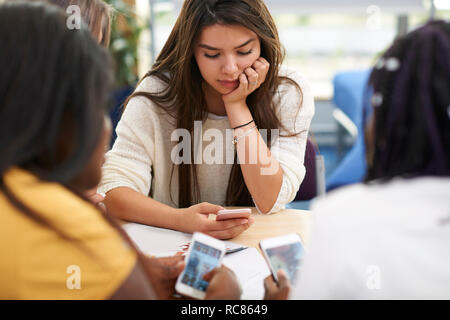 Female higher education students looking at smartphones in college classroom Stock Photo