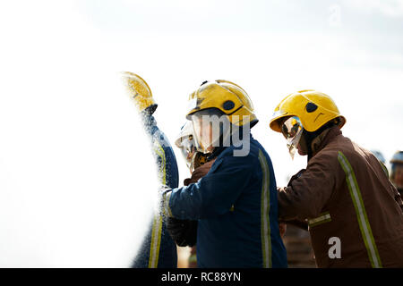 Firemen covered by water spray from fire hose Stock Photo
