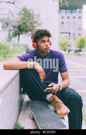 Skateboarder using headphones on concrete bench, Milan, Italy Stock Photo