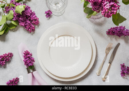Spring elegant table place setting with lilac flowers, silverware on light table. Top view. Stock Photo