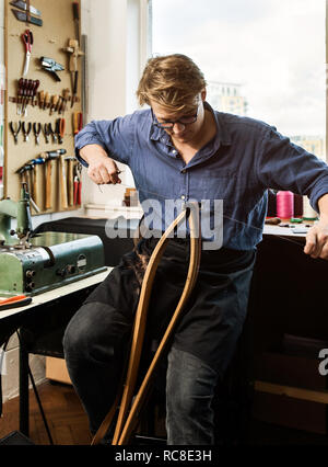 Leatherworker stitching leather handbag straps in workshop Stock Photo