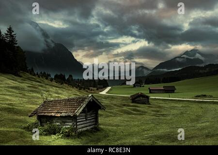 Small huts on mountain meadow with dramatic cloud sky and Wetterstein mountains in the background, Mittenwald, Bavaria, Germany Stock Photo
